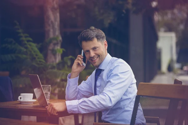 Retrato de homem de negócios falando no telefone celular enquanto usa laptop — Fotografia de Stock