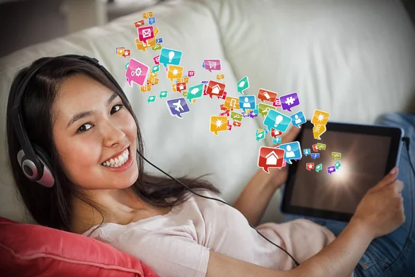 Mädchen mit ihrem Tablet-PC auf dem Sofa und Musik hören lächelnd in die Kamera 3d — Stockfoto