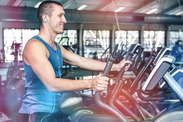 Hombre musculoso sonriente usando máquina elíptica —  Fotos de Stock