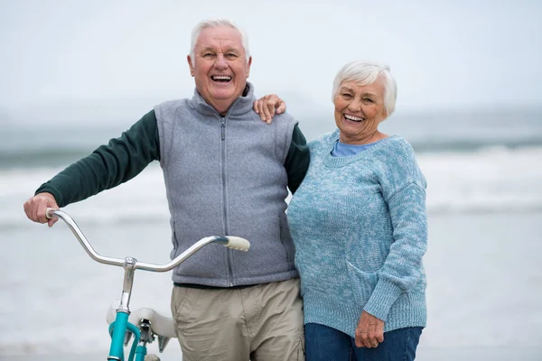 Coppia anziana in piedi con bicicletta sulla spiaggia — Foto Stock