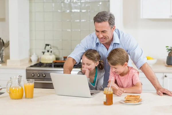 Отец и его дети за завтраком пользуются ноутбуком — стоковое фото