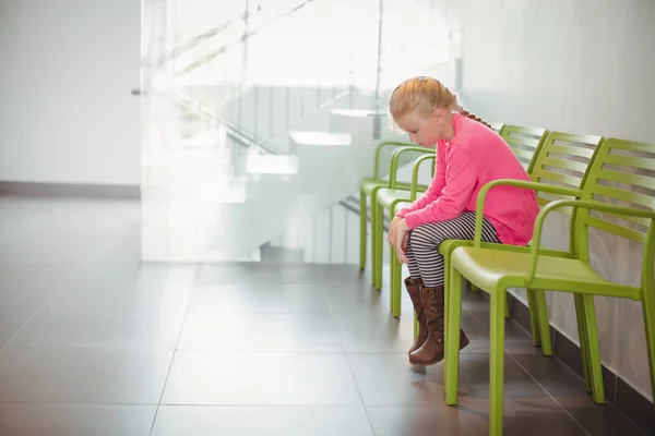 Upprörd tjej sitter på stol i korridor — Stockfoto