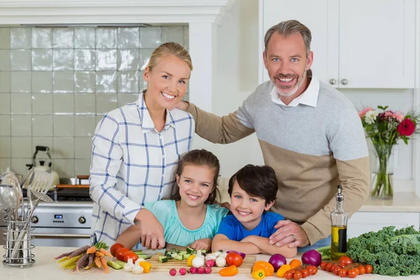 Улыбающиеся родители и дети рубят овощи на кухне — стоковое фото