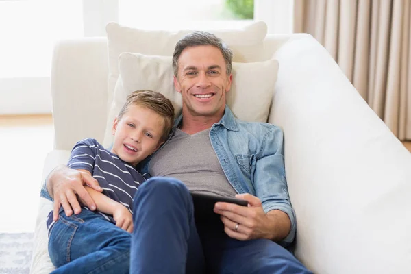 Père et fils couchés sur canapé avec tablette numérique dans le salon — Photo