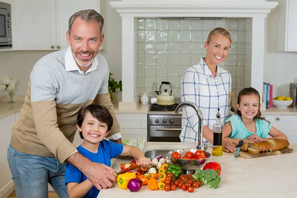 Des parents souriants aident un enfant à hacher des légumes dans la cuisine — Photo