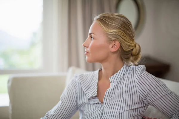 Thoughtful woman sitting on sofa in living room — Stock Photo, Image