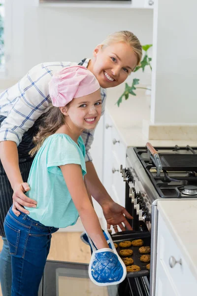 Feliz madre e hija colocando bandeja de galletas en el horno — Foto de Stock