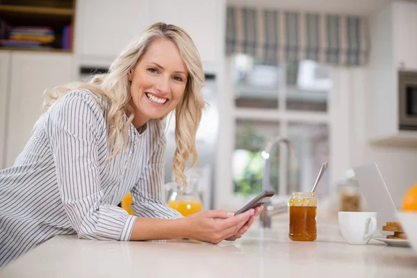 Όμορφη γυναίκα που χρησιμοποιούν κινητό τηλέφωνο στην κουζίνα — Φωτογραφία Αρχείου