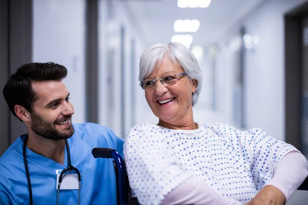 Arzt interagiert mit Seniorin im Rollstuhl auf dem Flur — Stockfoto