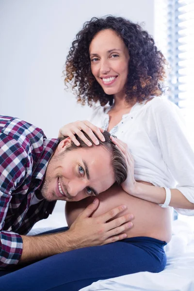 Sonriente hombre escuchando a las mujeres embarazadas vientre en la sala —  Fotos de Stock