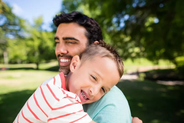 Filho sorrindo enquanto abraça seu pai no parque — Fotografia de Stock