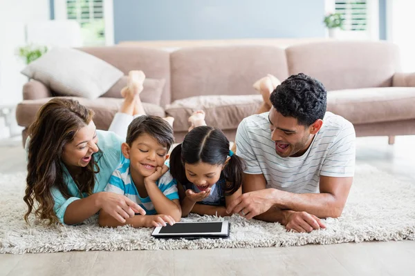 Föräldrar och barn liggande på matta och använda digitala surfplatta i vardagsrum — Stockfoto