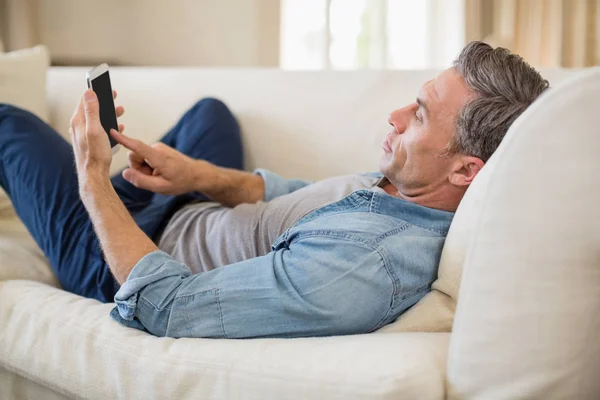 Мужчина лежит на диване и использует мобильный телефон в гостиной — стоковое фото