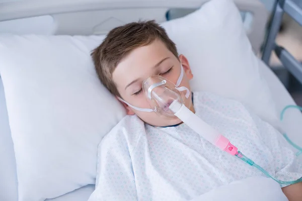 Boy patient wearing oxygen mask lying on hospital bed — Stock Photo, Image