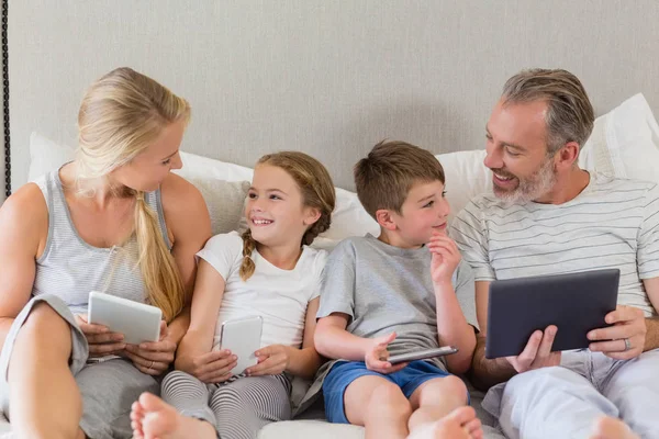 Padres e hijos interactuando mientras usan la tableta digital en la cama —  Fotos de Stock