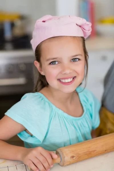 自宅の台所で麺棒とシェフの帽子をかぶって微笑んでいる女の子 — ストック写真