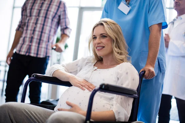 Médico masculino empurrando uma mulher grávida na cadeira de rodas — Fotografia de Stock