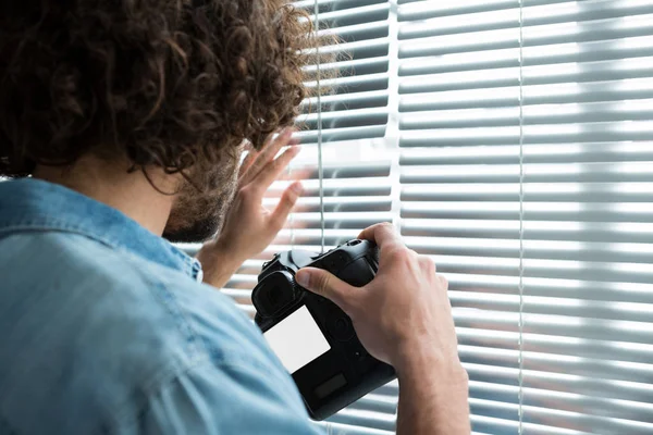 Photographer looking through window blinds — Stock Photo, Image