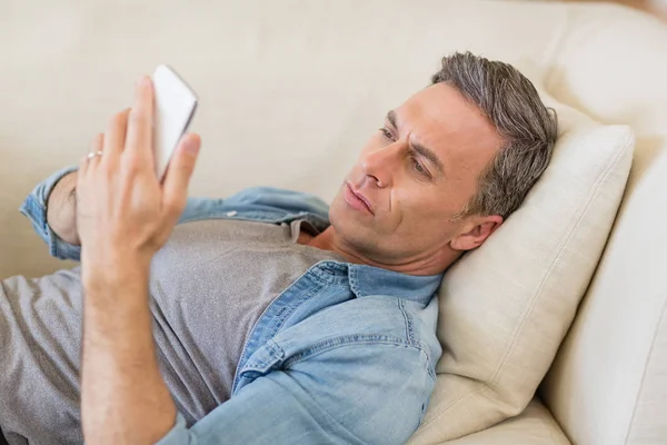 Man lying on sofa and using mobile phone in living room — Stock Photo, Image