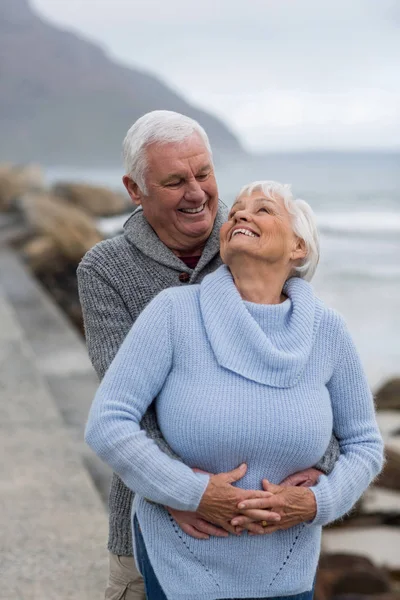 Äldre par omfamnar varandra på stranden — Stockfoto