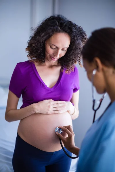 Doctor examining pregnant womans belly with stethoscope in ward — Stock Photo, Image