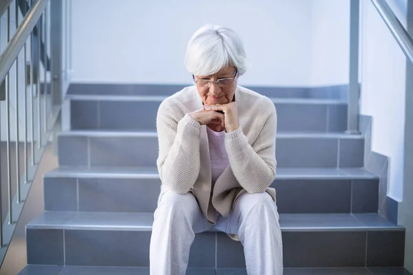 Расстроенная пожилая женщина сидит на лестнице — стоковое фото
