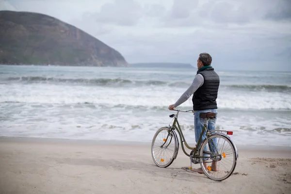 Dojrzały człowiek stojący z rowerem na plaży — Zdjęcie stockowe