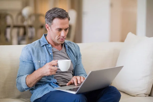 Man met laptop terwijl het hebben van koffie in de woonkamer — Stockfoto