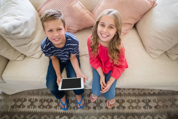 微笑着坐在沙发上与数字平板电脑在客厅里的兄弟姐妹 — 图库照片