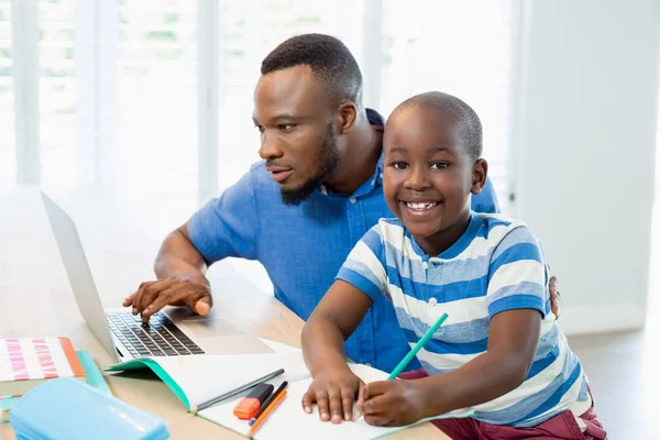 Père utilisant un ordinateur portable et son fils faisant ses devoirs dans le salon — Photo