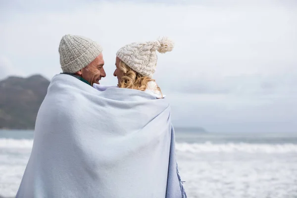 Äldre par insvept i filt på stranden — Stockfoto