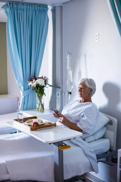 Kvinnliga senior patienten använda mobiltelefon på säng — Stockfoto