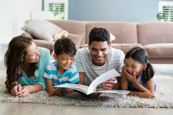 Padres e hijos acostados en una alfombra y leyendo un libro en la sala de estar —  Fotos de Stock