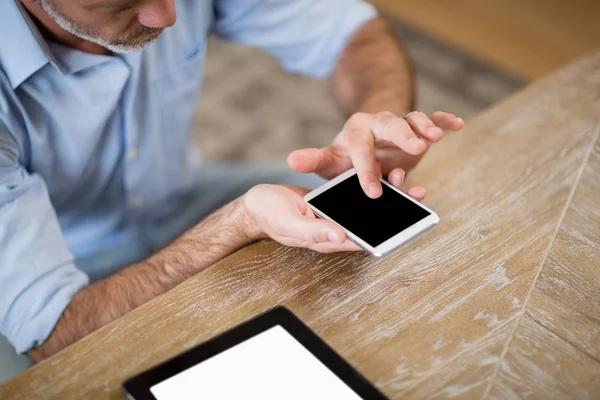 Hombre usando teléfono móvil con tableta digital en la mesa en la sala de estar — Foto de Stock