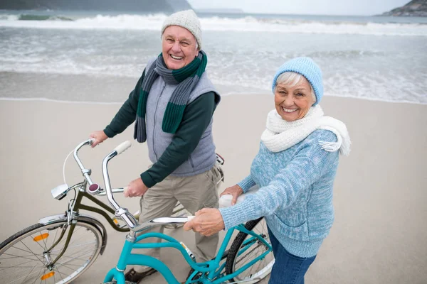 Portret van senior paar staande met fietsen op het strand — Stockfoto