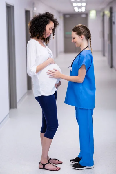 Doctor touching pregnant womans belly in corridor — Stock Photo, Image