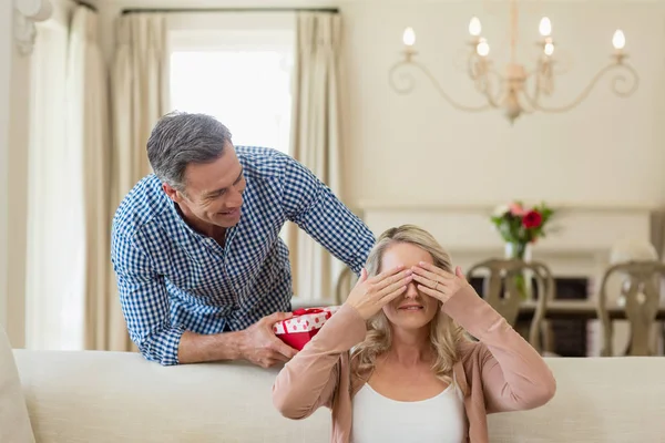 Hombre dando regalo sorpresa a la mujer en sala de estar — Foto de Stock