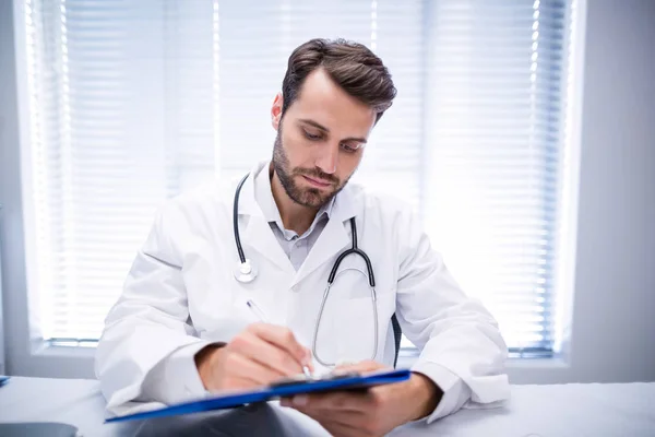 Male doctor writing on clipboard — Stock Photo, Image