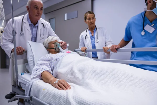 Médico e enfermeira empurrando cama maca de emergência no corredor — Fotografia de Stock