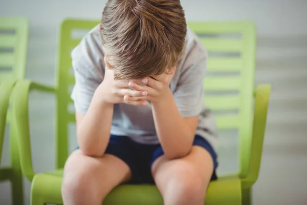 Расстроенный мальчик, сидящий на стуле в коридоре — стоковое фото