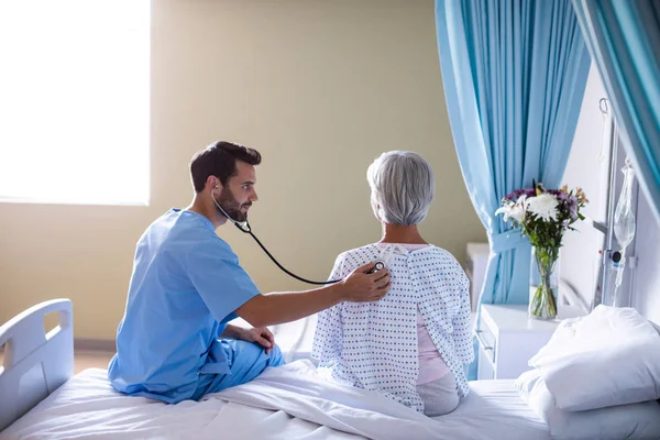 Médico masculino examinando a una paciente mayor con un estetoscopio — Foto de Stock