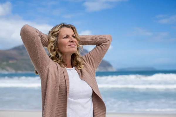 Zralá žena s rukama za hlavou stojící na pláži — Stock fotografie