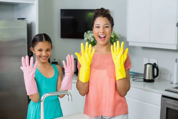 Retrato de filha e mãe mostrando luvas na cozinha — Fotografia de Stock