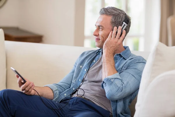 Muž poslouchá hudbu na sluchátkách v obývacím pokoji — Stock fotografie
