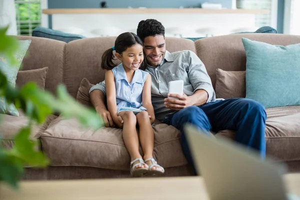 Батько і дочка сидять на дивані і використовують мобільний телефон — стокове фото