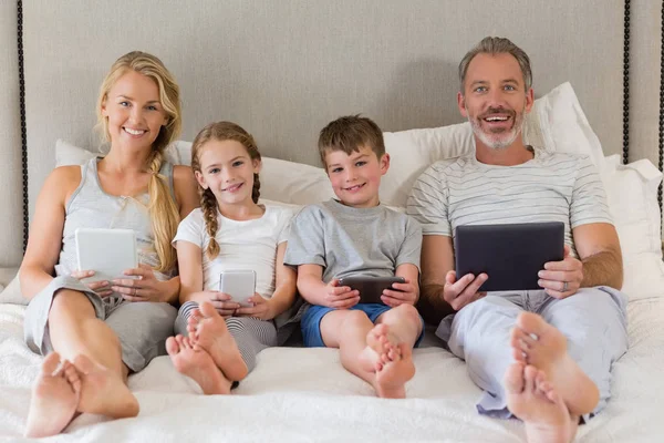 Родители и дети с помощью мобильного телефона и цифрового планшета на кровати — стоковое фото