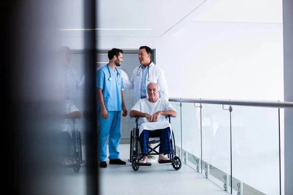 Médicos interactuando entre sí con el paciente en silla de ruedas en el pasillo —  Fotos de Stock