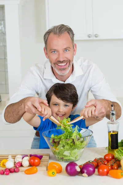 Sonriente padre e hijo preparando ensalada en la cocina en casa —  Fotos de Stock