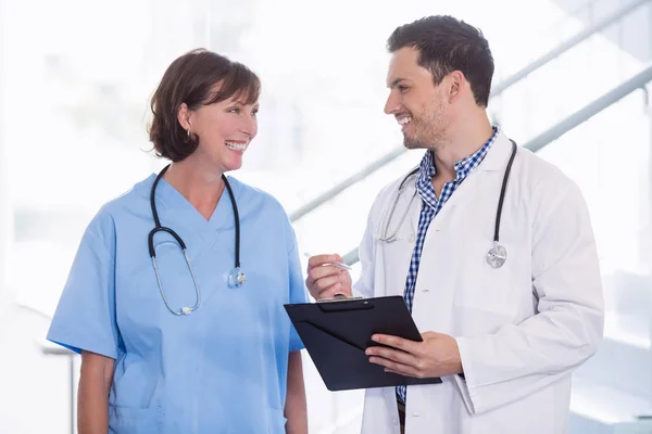 Enfermera y médico discutiendo sobre portapapeles en el pasillo —  Fotos de Stock
