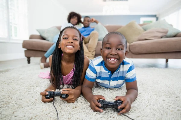Братья и сёстры лежат на ковре и играют в видеоигры — стоковое фото